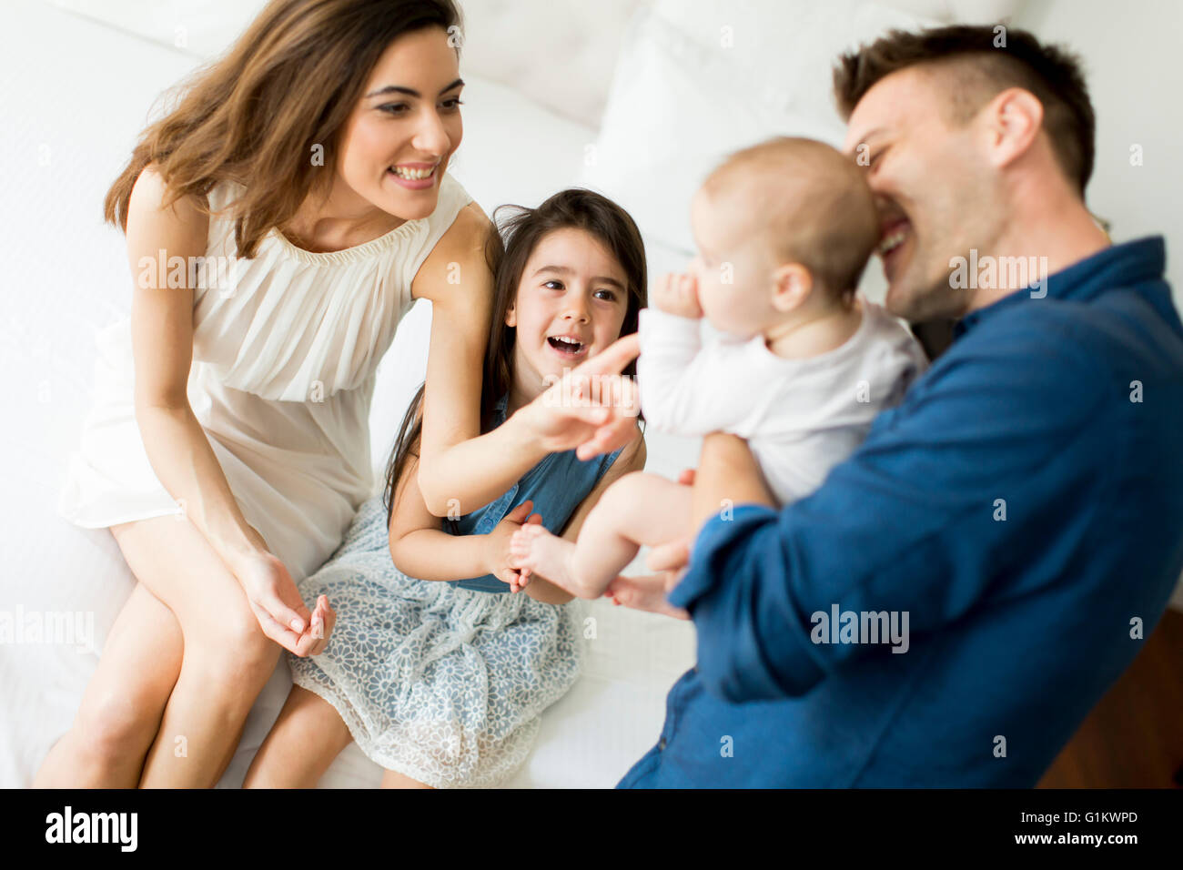 Felice giovani genitori seduti su un letto con una bambina e baby Foto Stock