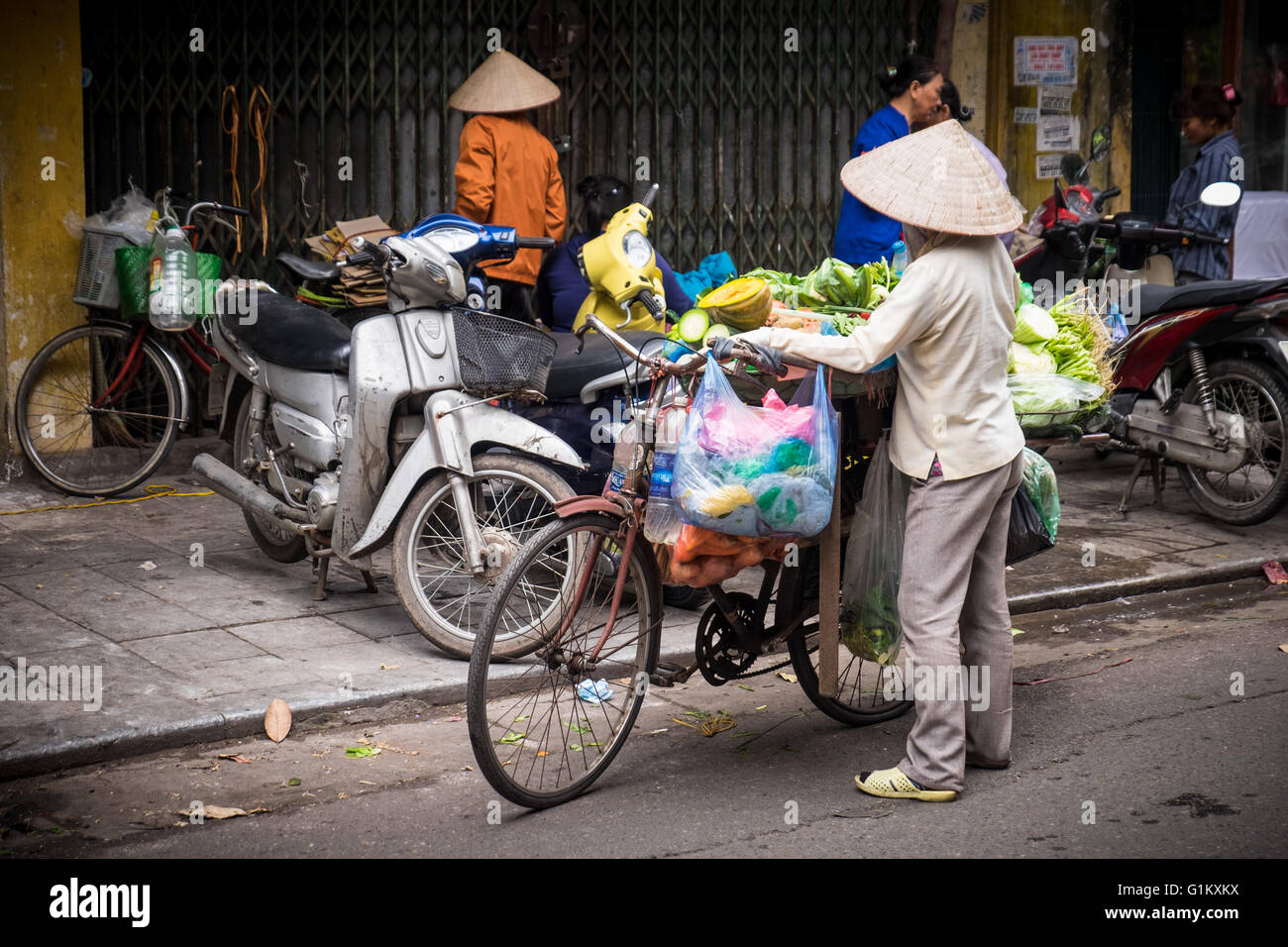 Una donna vendita di prodotti freschi dalla sua bicicletta nella città vecchia di Hanoi e il Vietnam Foto Stock