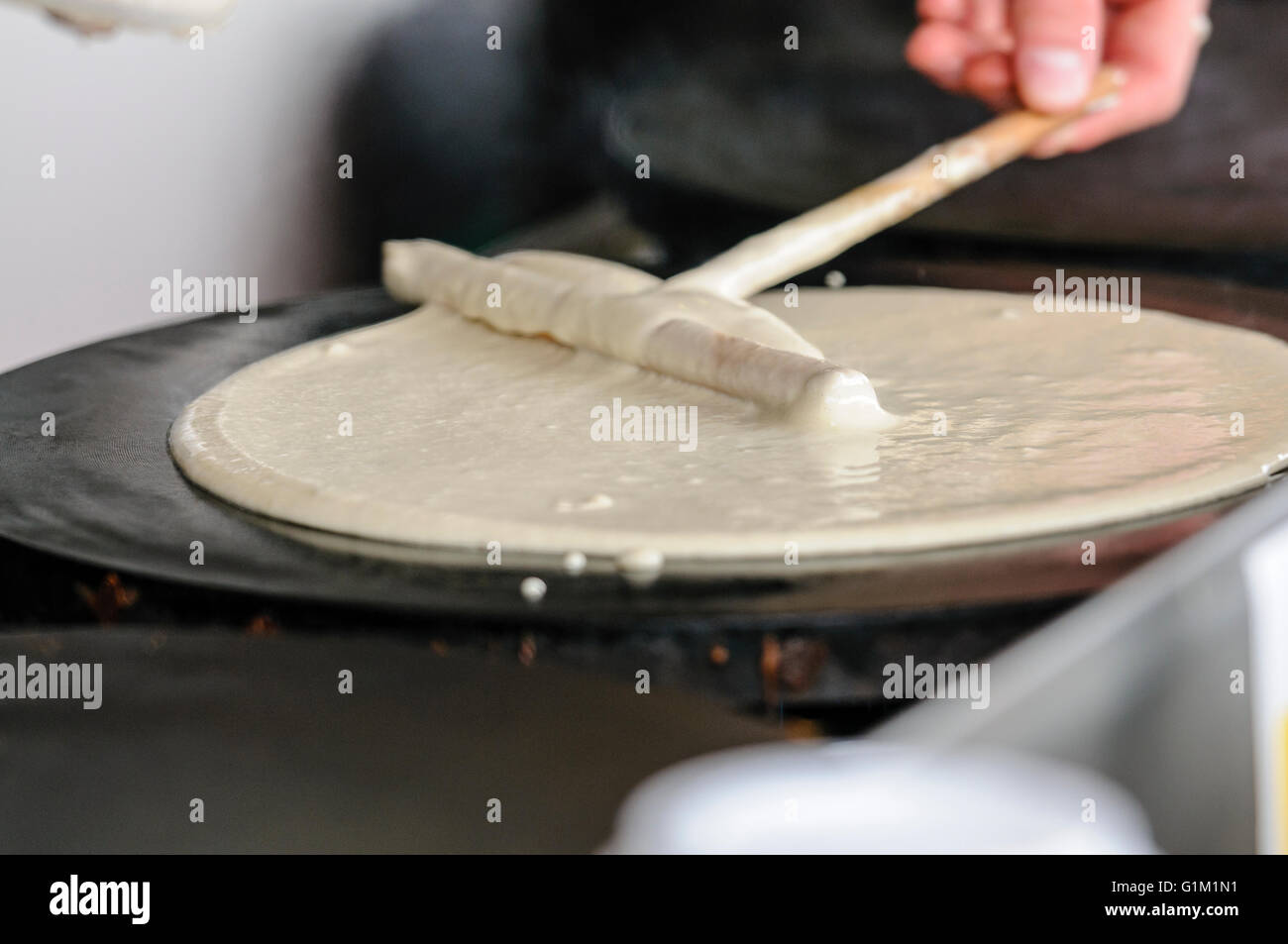 Un uomo si diffonde la pastella sulla piastra riscaldante per rendere le crepes. Foto Stock