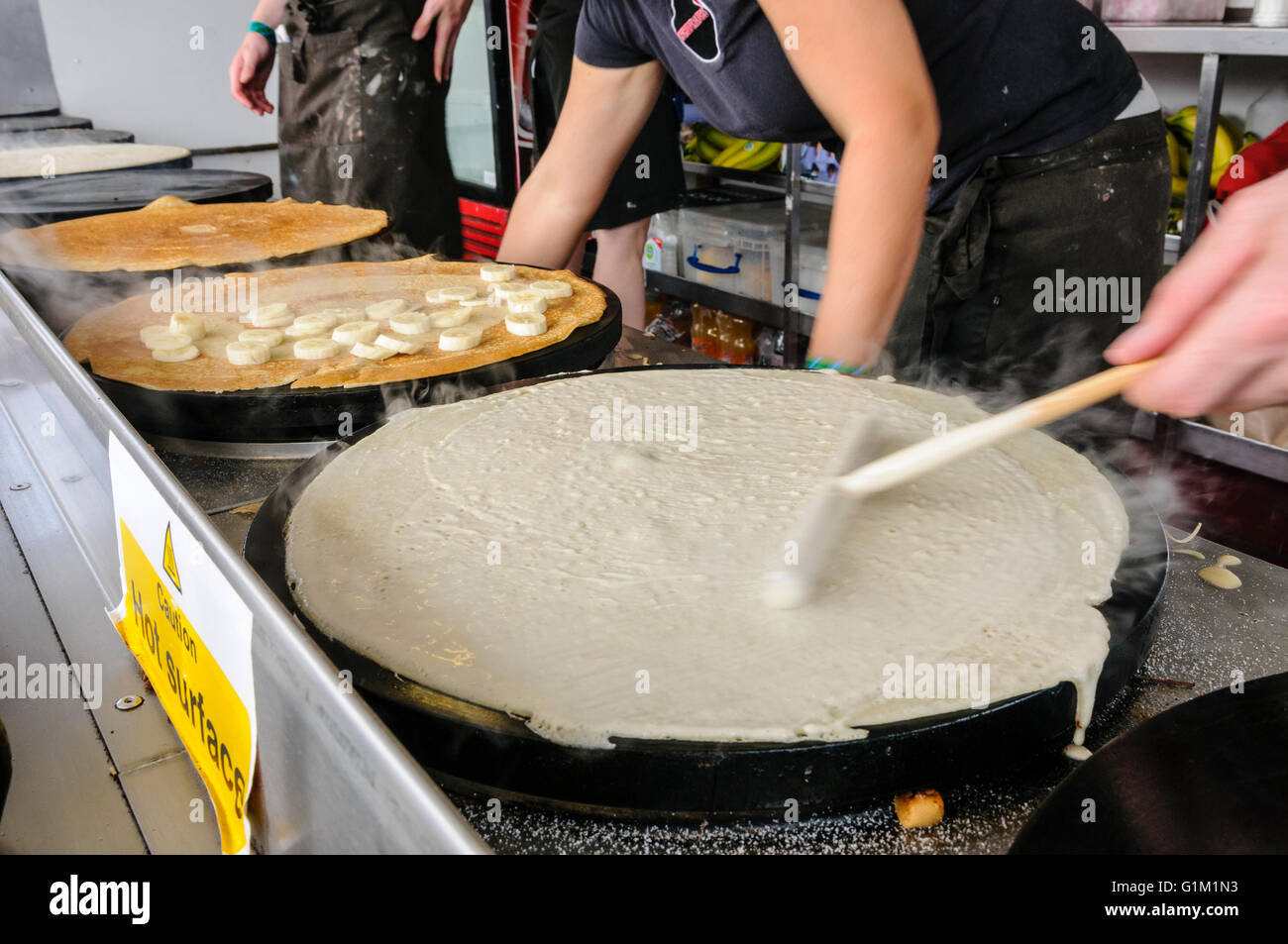 Un uomo si diffonde la pastella sulla piastra riscaldante per rendere le crepes. Foto Stock