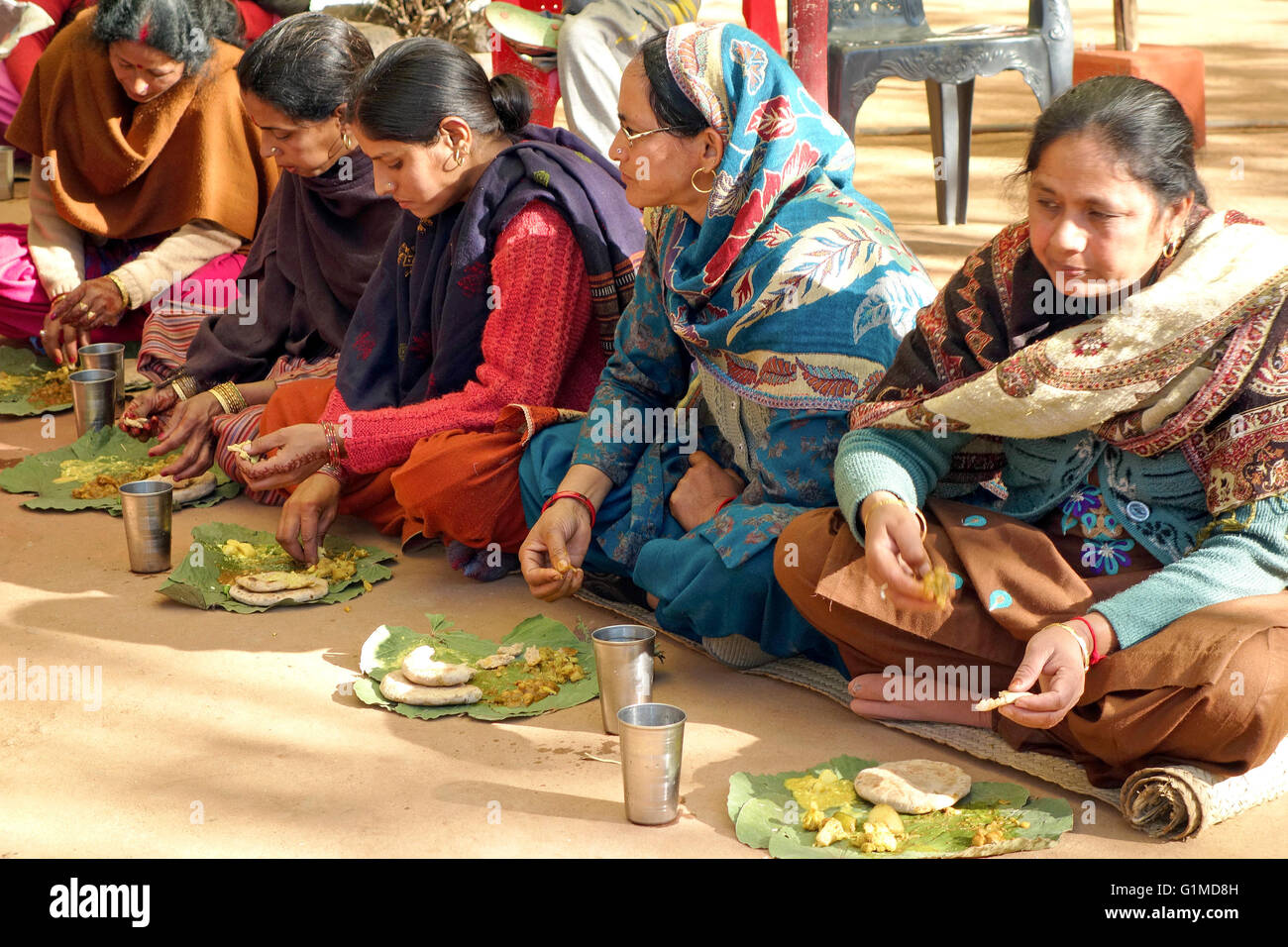 Le persone sedute a terra e mangiare mangiare insieme ad una cerimonia di nozze tradizionale a Himichal Pradesh, India Foto Stock