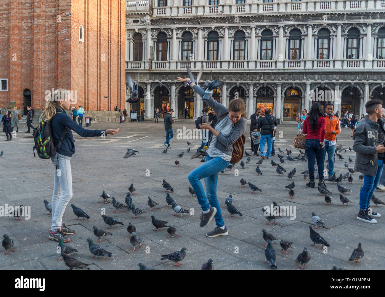 Giovani turisti giocando con / alimentazione di piccioni in Piazza San Marco, Venezia Foto Stock