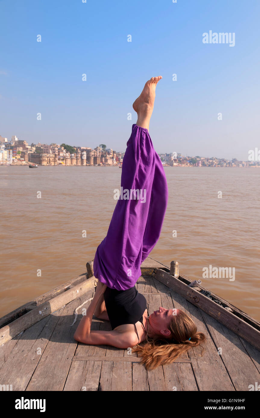 Giovane femmina la pratica dello yoga pongono Sarvangasana sulle barche sul fiume Ganga, India Foto Stock