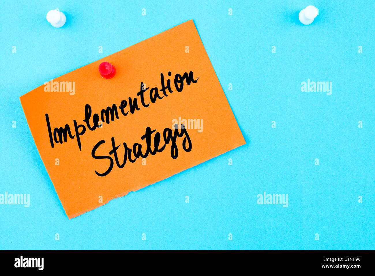 Strategia di implementazione scritta sulla carta arancione nota appuntata sulla bacheca di sughero con la puntina bianca, copia dello spazio disponibile Foto Stock