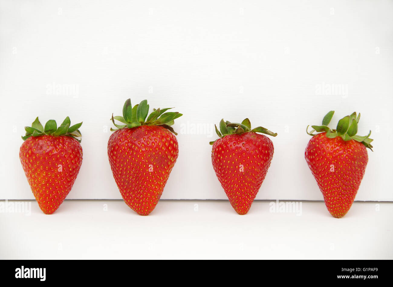 Rosso fragole con steli verdi disposti in uno sfondo bianco Foto Stock