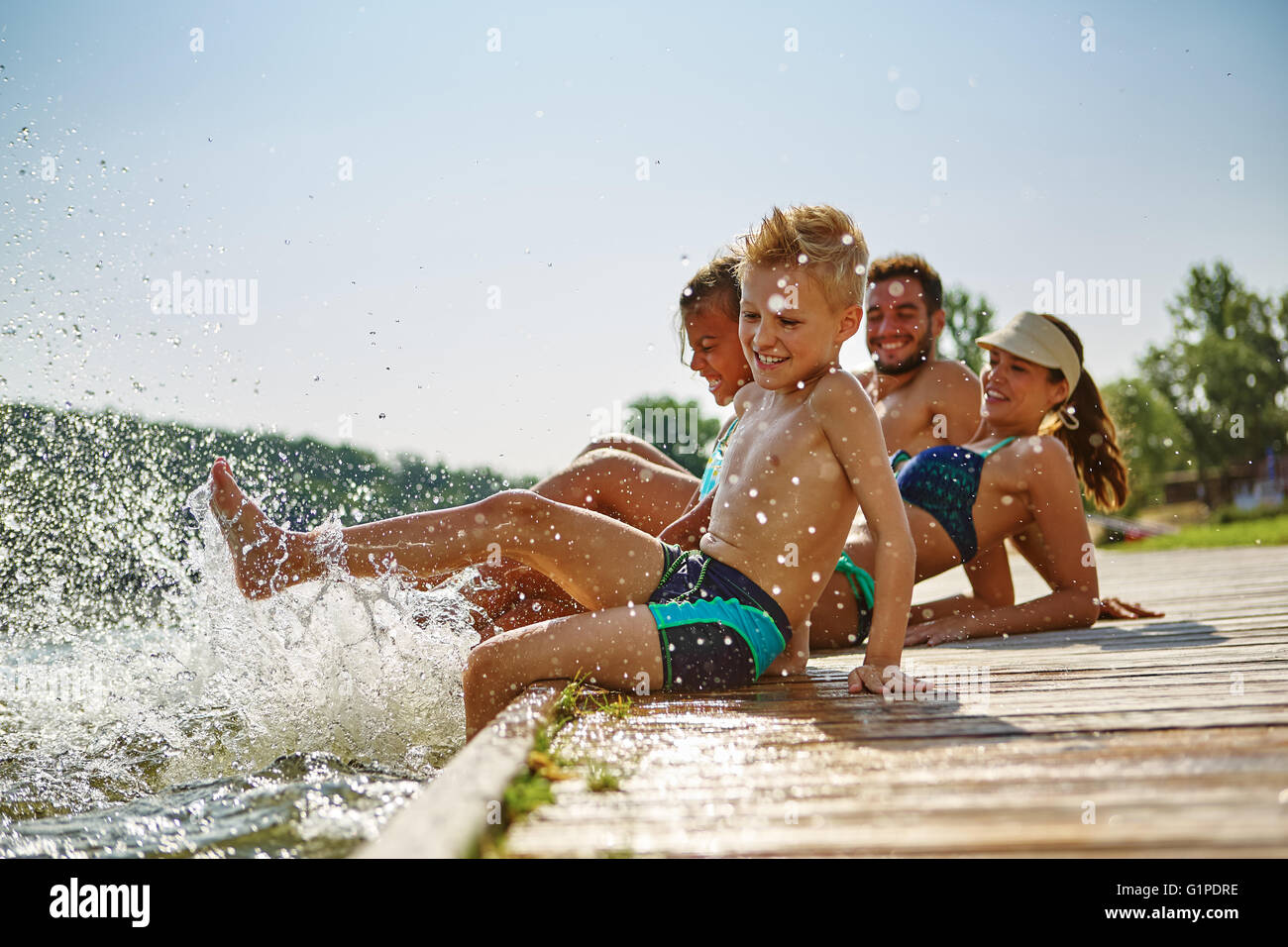 La famiglia felice divertendosi e spruzzi d'acqua con i piedi su un lago Foto Stock