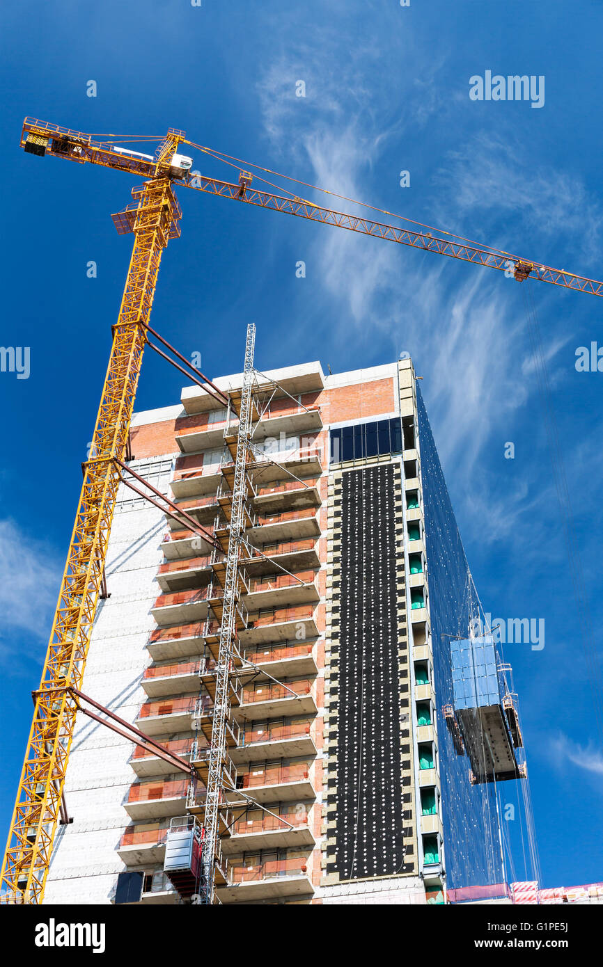 Un alto edificio in costruzione e la gru sotto il cielo blu Foto Stock