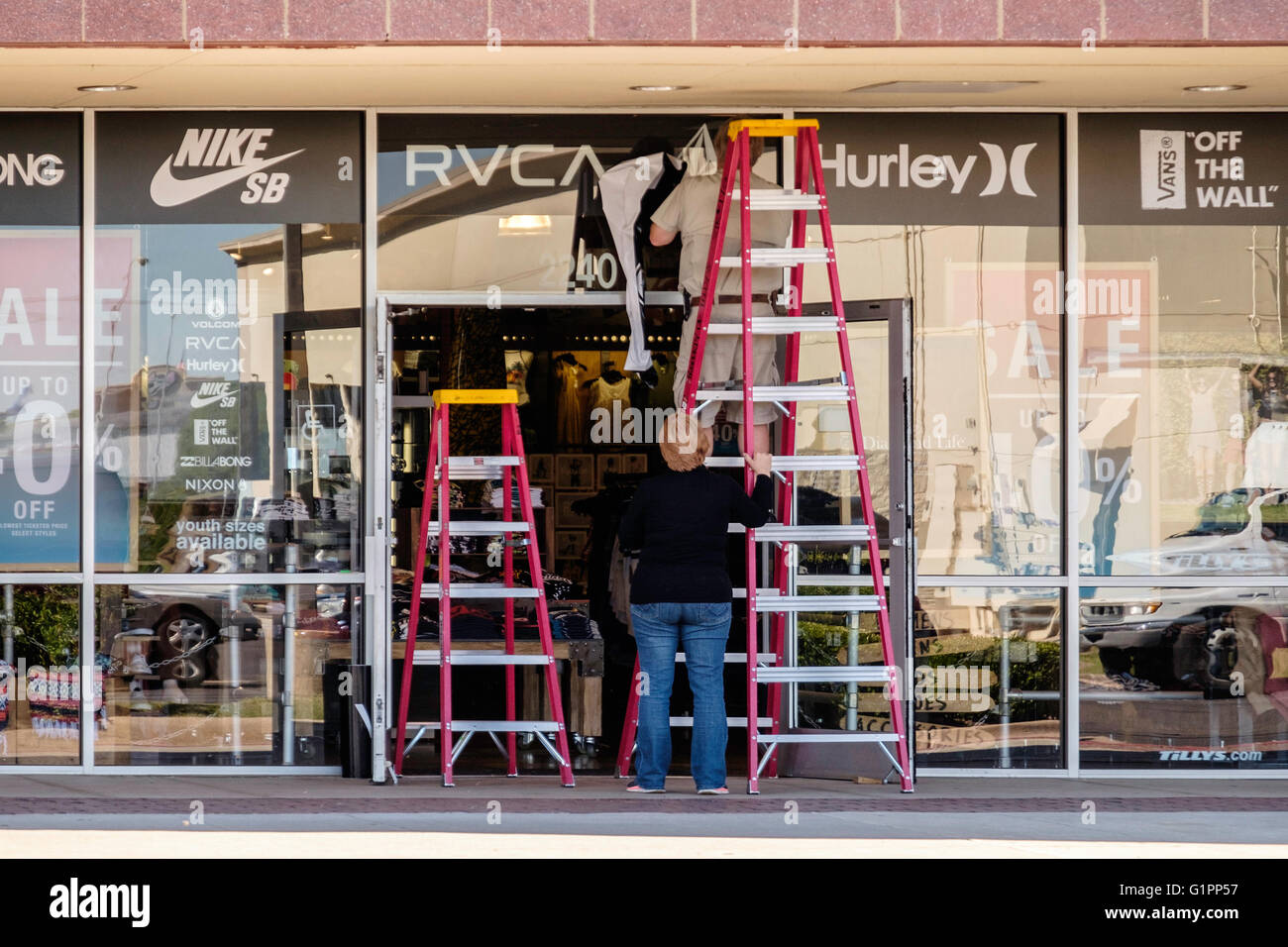Una donna caucasica corregge una scaletta mentre un uomo strisce a firmare da un negozio finestra. Oklahoma City, Oklahoma, Stati Uniti d'America. Foto Stock