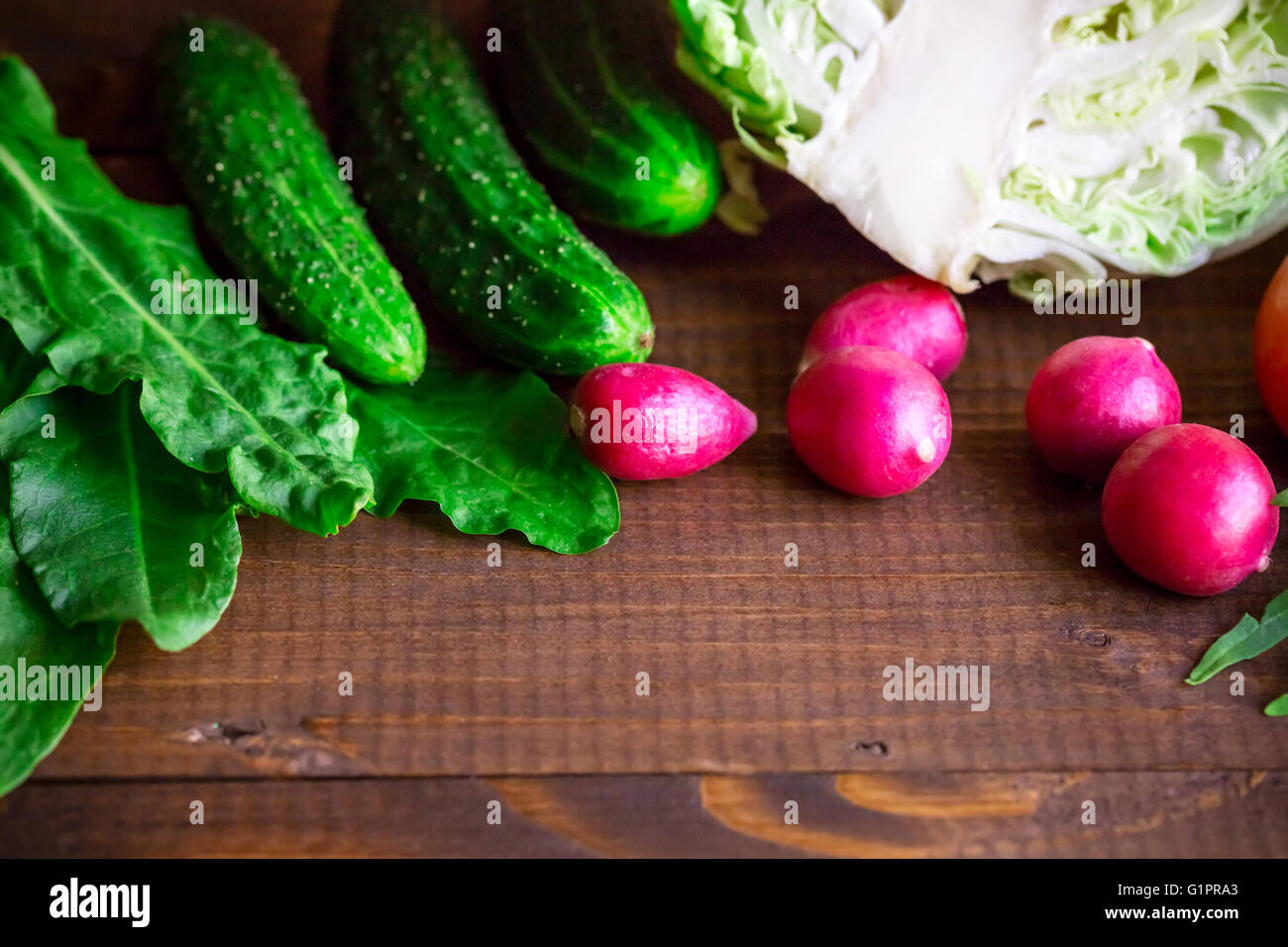 Sfondo con vecchie schede marrone con fresche verdure sane, il cipollotto, rafano, cetriolo, rucola e cavolo. spazio vuoto Foto Stock