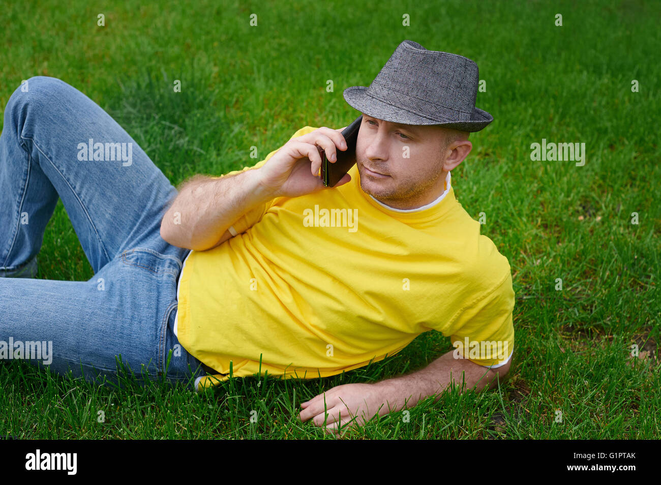 Smart giovane in un giallo T-shirt con il telefono sull'erba Foto Stock
