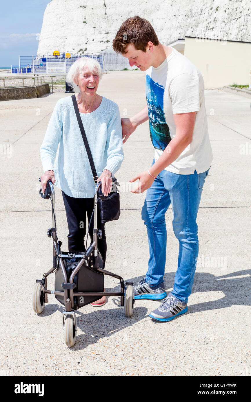 Un'anziana donna disabile utilizzando un Rollator aiuti a piedi aiutato da suo nipote, Brighton, Sussex, Regno Unito Foto Stock