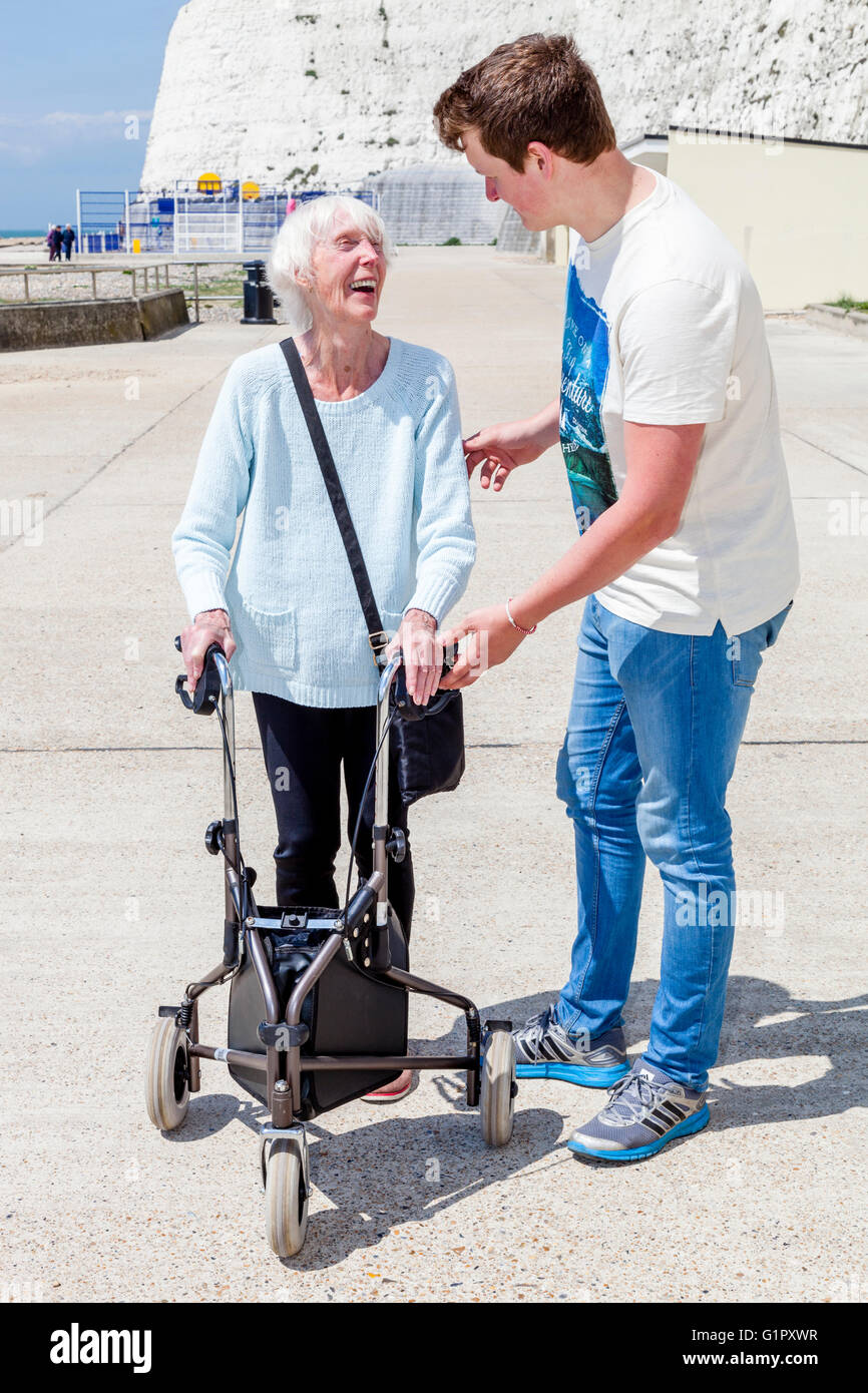 Un'anziana donna disabile utilizzando un Rollator aiuti a piedi aiutato da suo nipote, Brighton, Sussex, Regno Unito Foto Stock