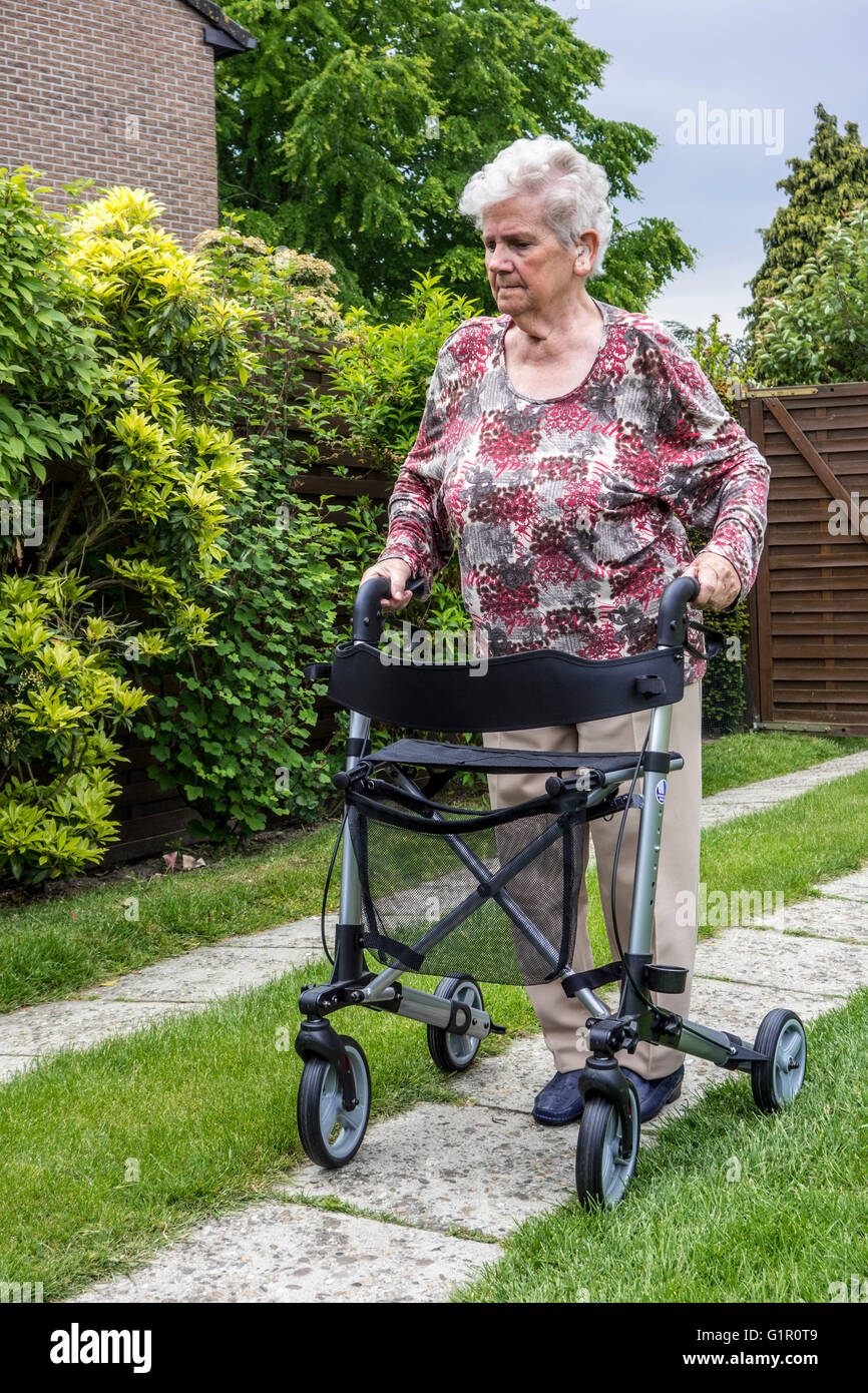 Donna anziana con rollator ruote / walker praticare passeggiate sul viale di accesso a casa Foto Stock