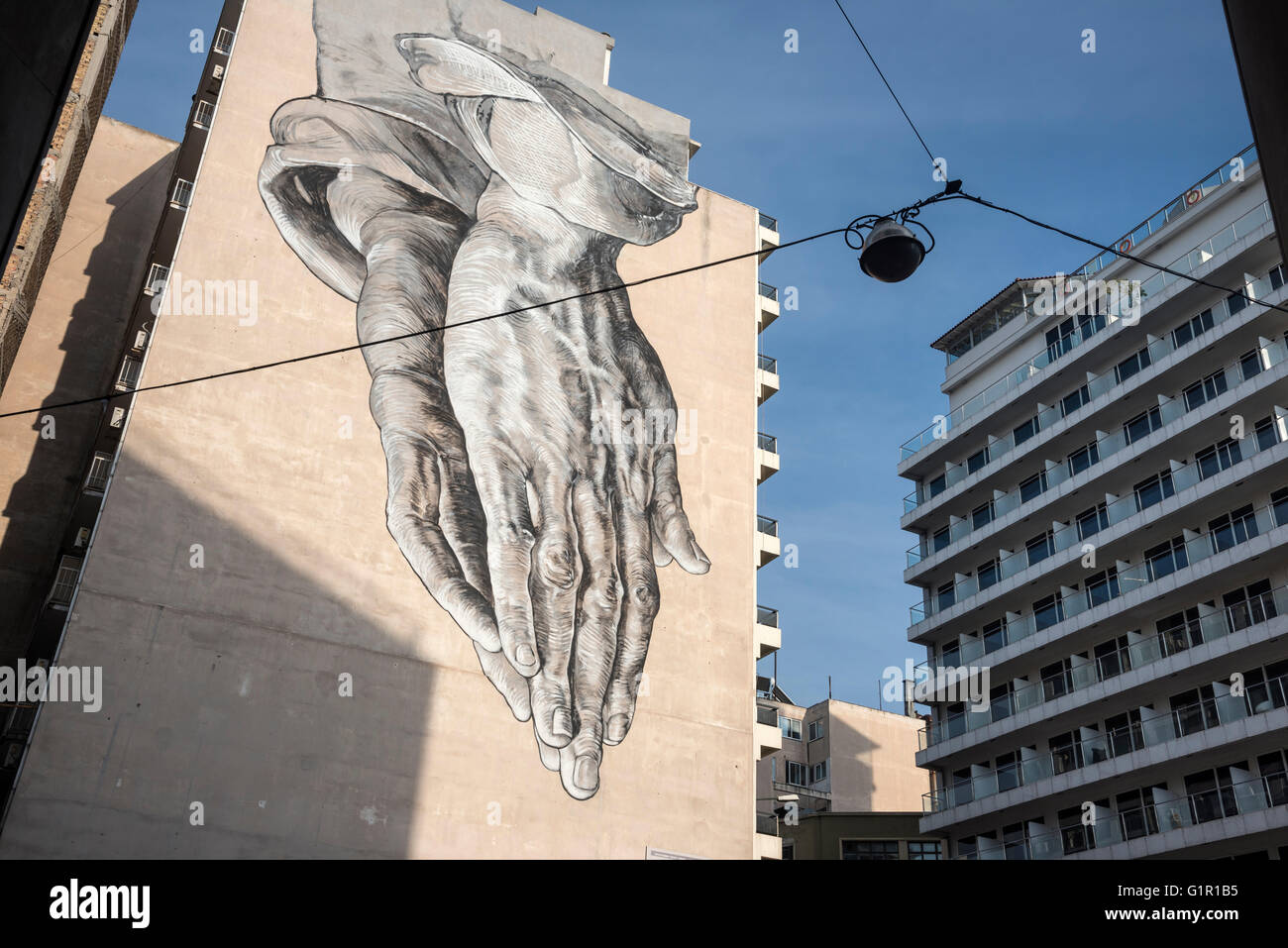 Un arte di strada murale in forma di un gigante di coppia di pregare telai a mano sulla Pireos street nel quartiere di Omonia di Atene, Grecia Foto Stock