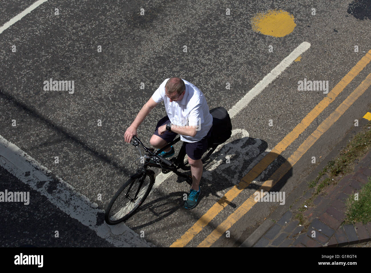Uomo di mezza età ciclista bike guardando guarda su un angolo della città di traffico in attesa di luce visto dal di sopra, Glasgow, Scotland, Regno Unito Foto Stock