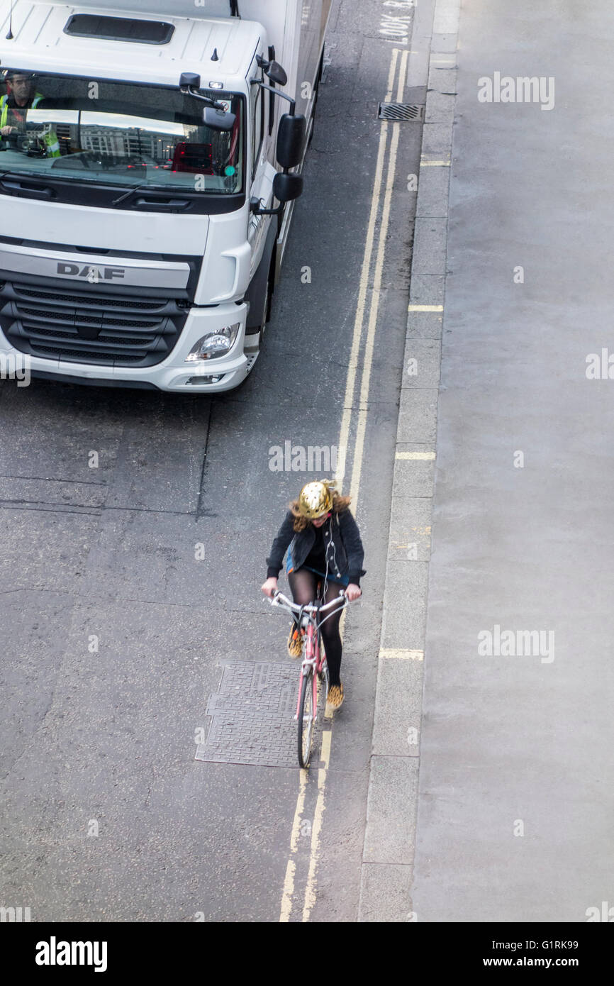 Ciclista maneggio vicino al marciapiede con un automezzo che si avvicina da dietro Foto Stock