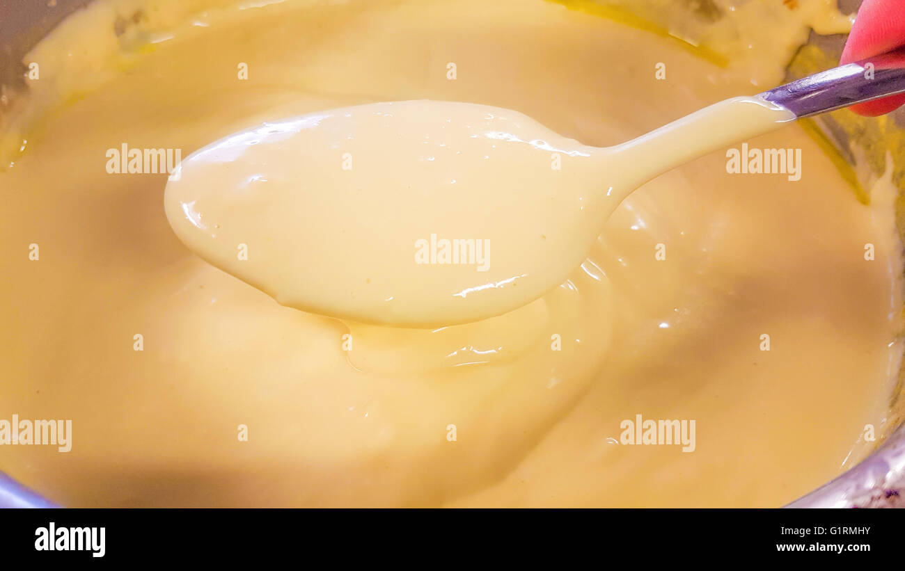 Cucchiaio colmo di salsa olandese, al di sopra di un casserol piena di più giallo salsa di burro Foto Stock