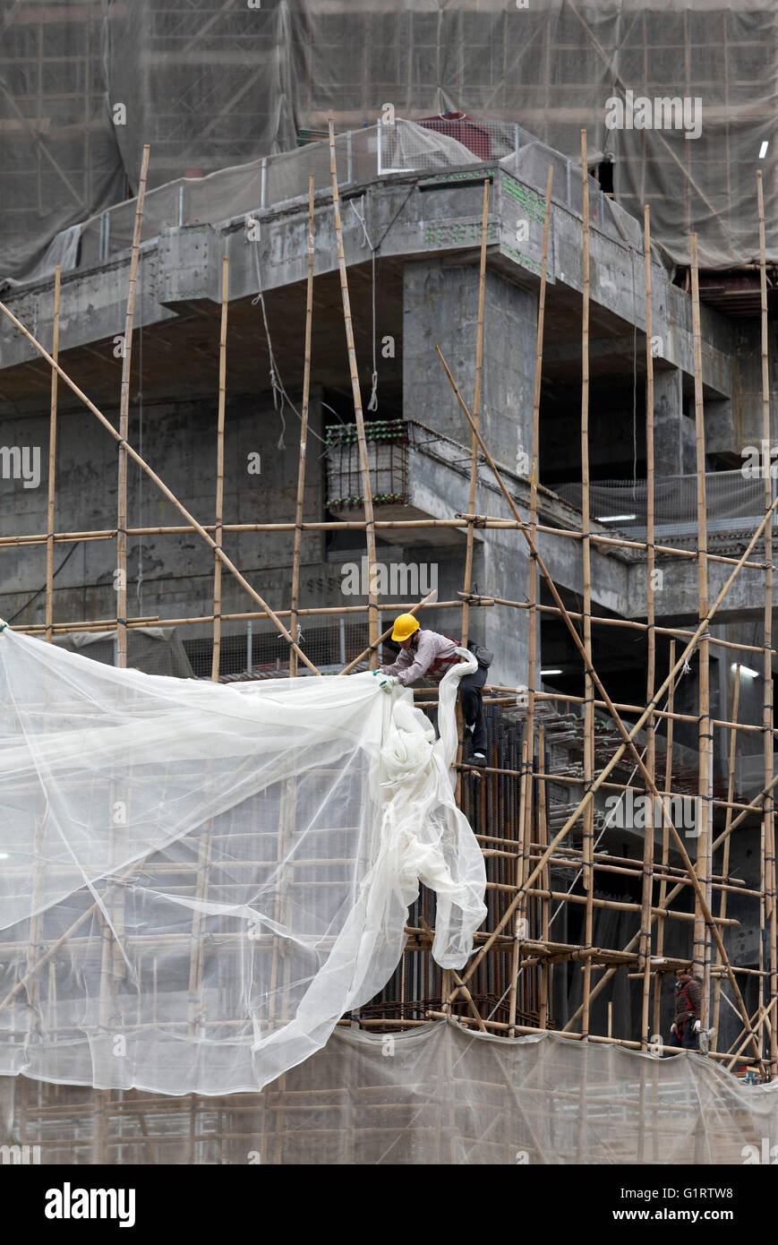 Lavoratori attaccato un telone di copertura di un ponteggio di bambù, alto edificio in costruzione, Tsim Sha Tsui, Kowloon Foto Stock