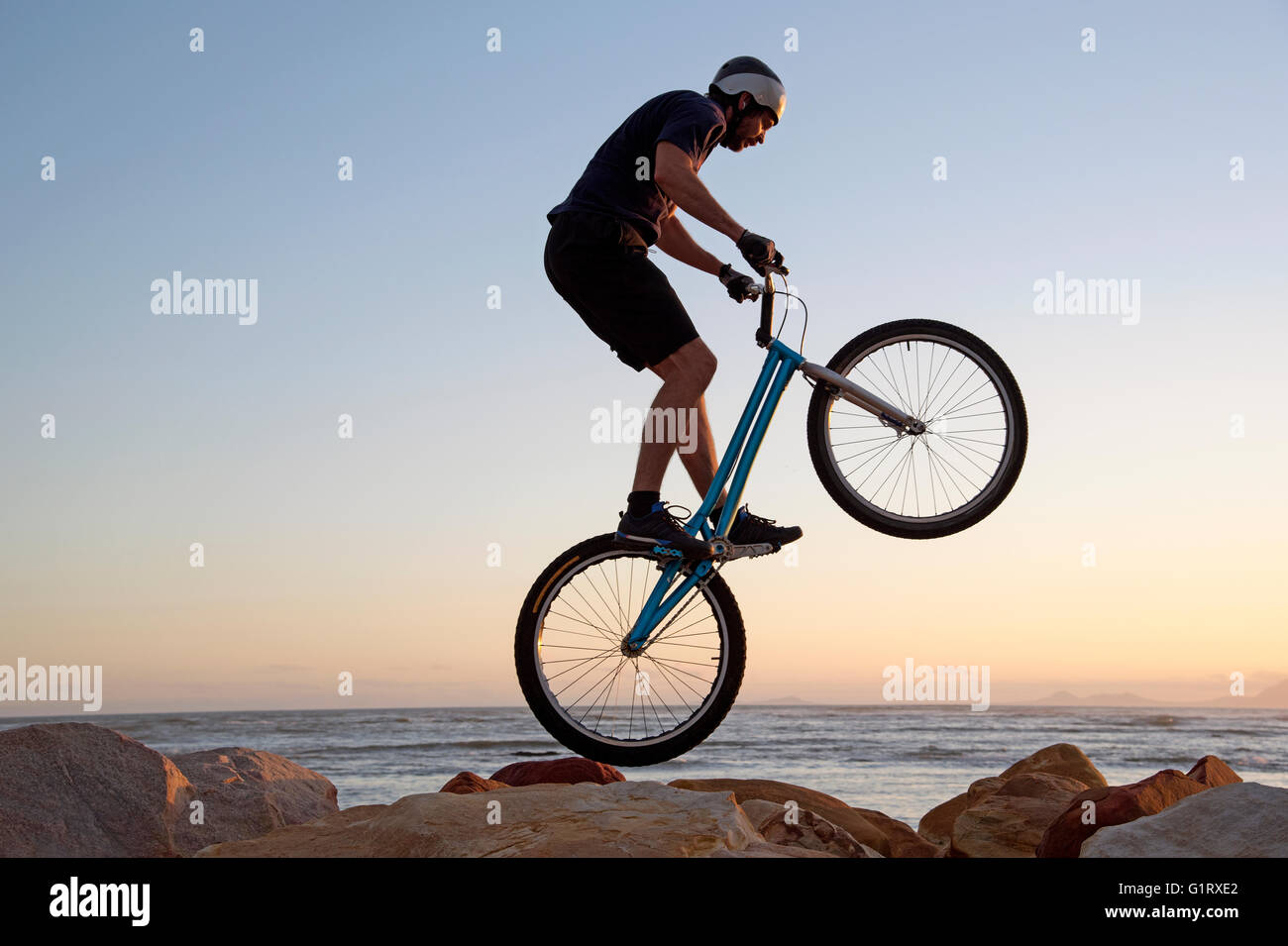 Il trefolo di Western Cape in Sud Africa. Una mountain bike rider abilmente a cavallo su rocce sulla battigia allo Strand Beach Foto Stock