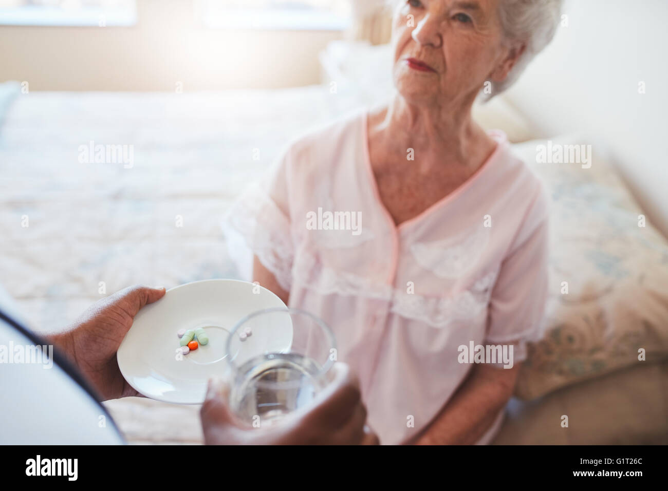 Senior donna seduta sul letto e home care nurse dando farmaco. La mano di infermiere dando pillole per anziani paziente femmina. Foto Stock