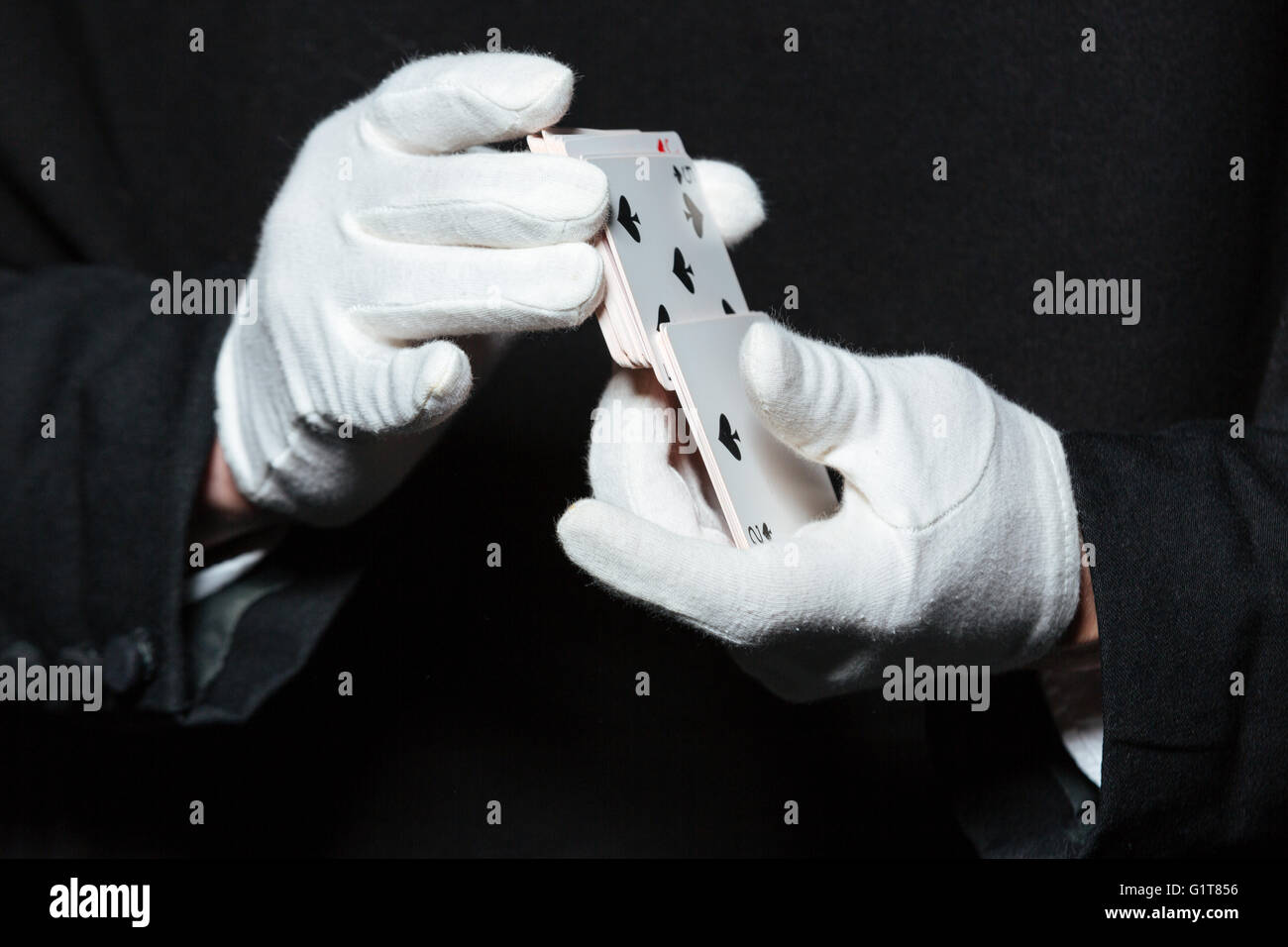 Primo piano delle mani dell'uomo mago in guanti bianchi rimescolare le carte da gioco su sfondo nero Foto Stock