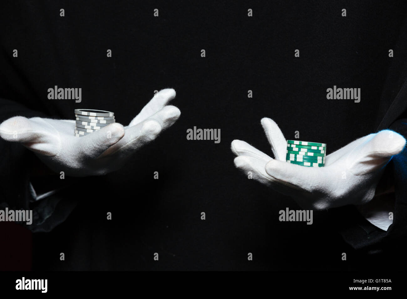 Primo piano delle mani dell'uomo mago in guanti bianchi azienda casino chips su entrambi i palmi su sfondo nero Foto Stock
