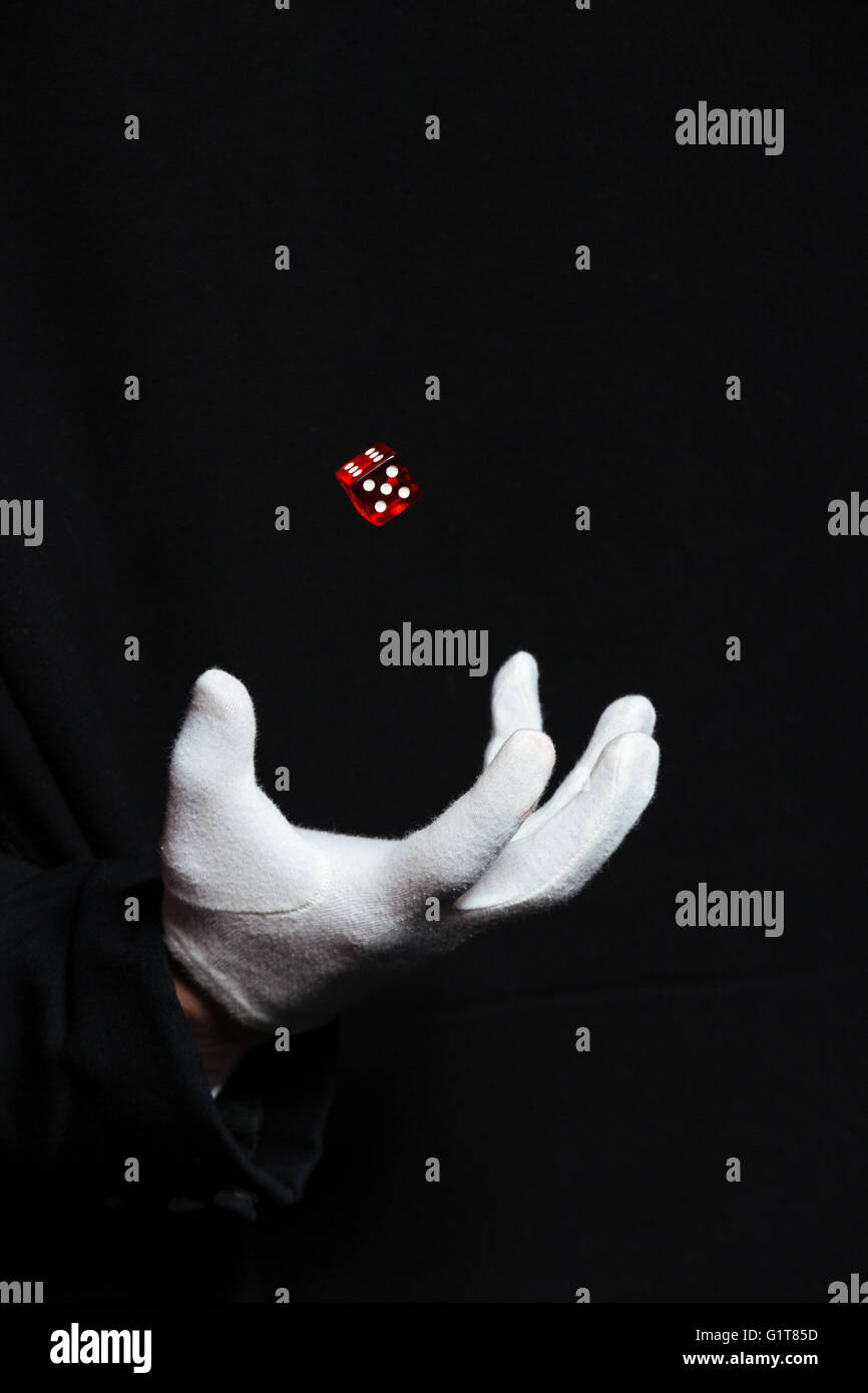 Mano di uomo mago in guanto bianco che mostra i trucchi utilizzando uno battenti dadi su sfondo nero Foto Stock