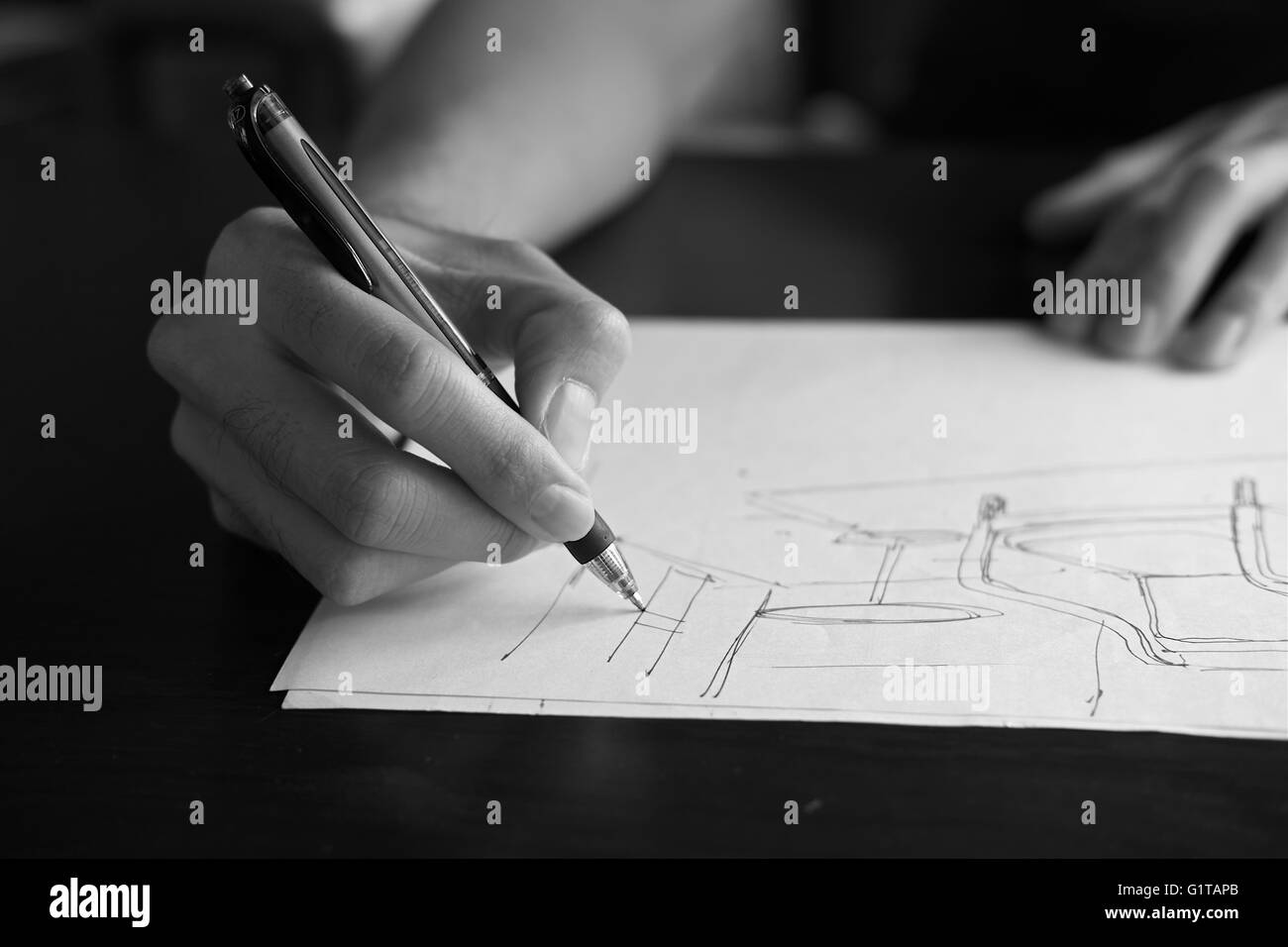 Mano di designer con la sua penna, progettando e delineando la sua idea su sketchbook in monocromia Foto Stock