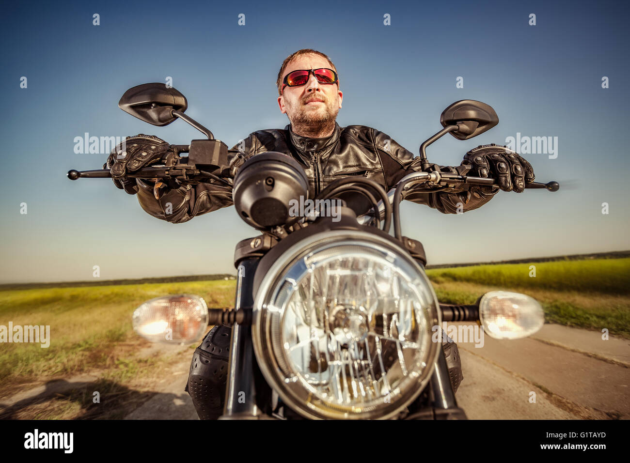 Biker in una giacca di pelle in sella a una motocicletta sulla strada. Filtro applicato in post-produzione. Foto Stock Biker in una giacca di pelle in sella a una motocicletta sulla strada. Filtro applicato in post-produzione. Foto Stock