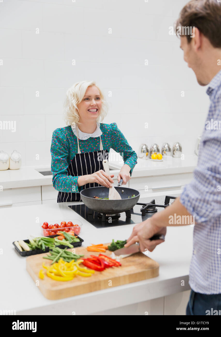 Coppia sorridente affettamento e cucina verdure in cucina Foto Stock
