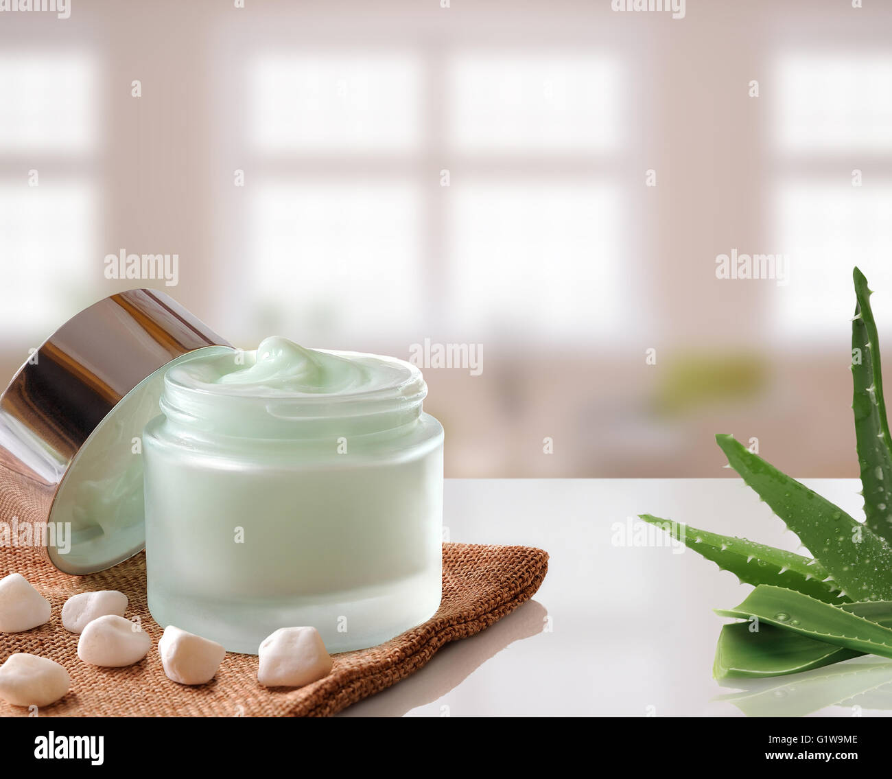 Vetro vaso aperto con trattamento viso o crema per il corpo Aloe vera su tela. Con coperchio, con piccole pietre e aloe.background Windows. Foto Stock