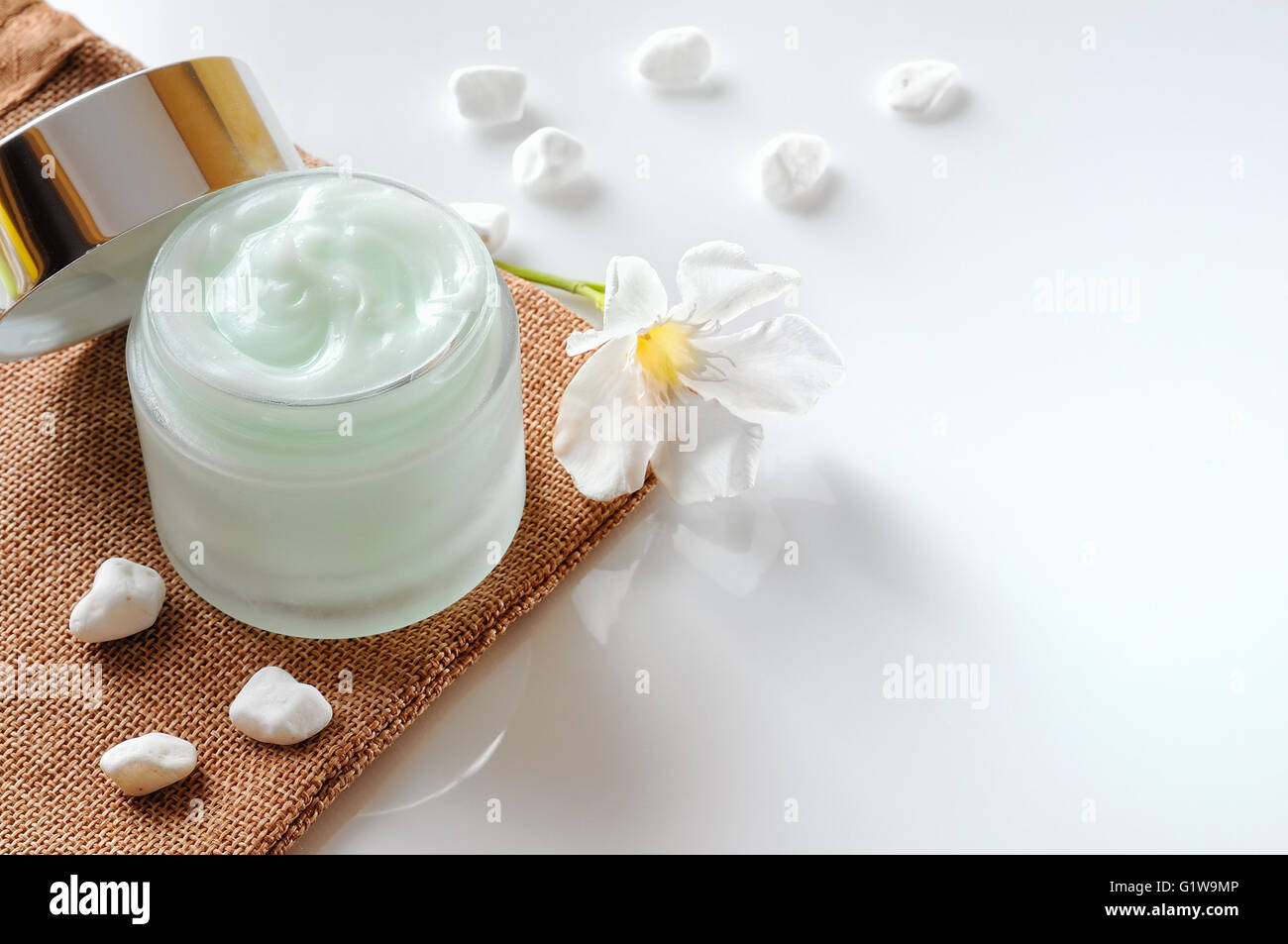 Vasetto di crema aperto sulla tela con pietre e fiori in cima isolata sul tavolo bianco Foto Stock