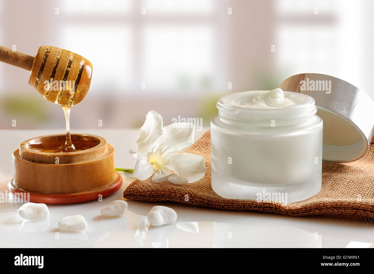 Aprire il vaso di vetro con miele idratante isolato su bianco tavolo in vetro. Fiore, pietre, tela e la canna da zucchero con miele decor di contenitore Foto Stock
