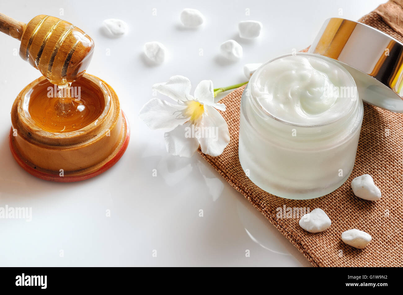 Aprire il vaso di vetro con miele idratante isolato su bianco tavolo in vetro. Fiore, pietre, tela e la canna da zucchero con miele decor di contenitore Foto Stock
