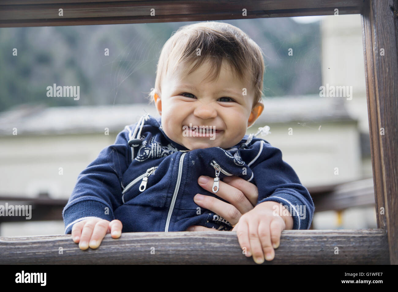 Graziosa piccola di un anno di età del bambino a sorridente telecamera tenendo recinzione di legno Foto Stock
