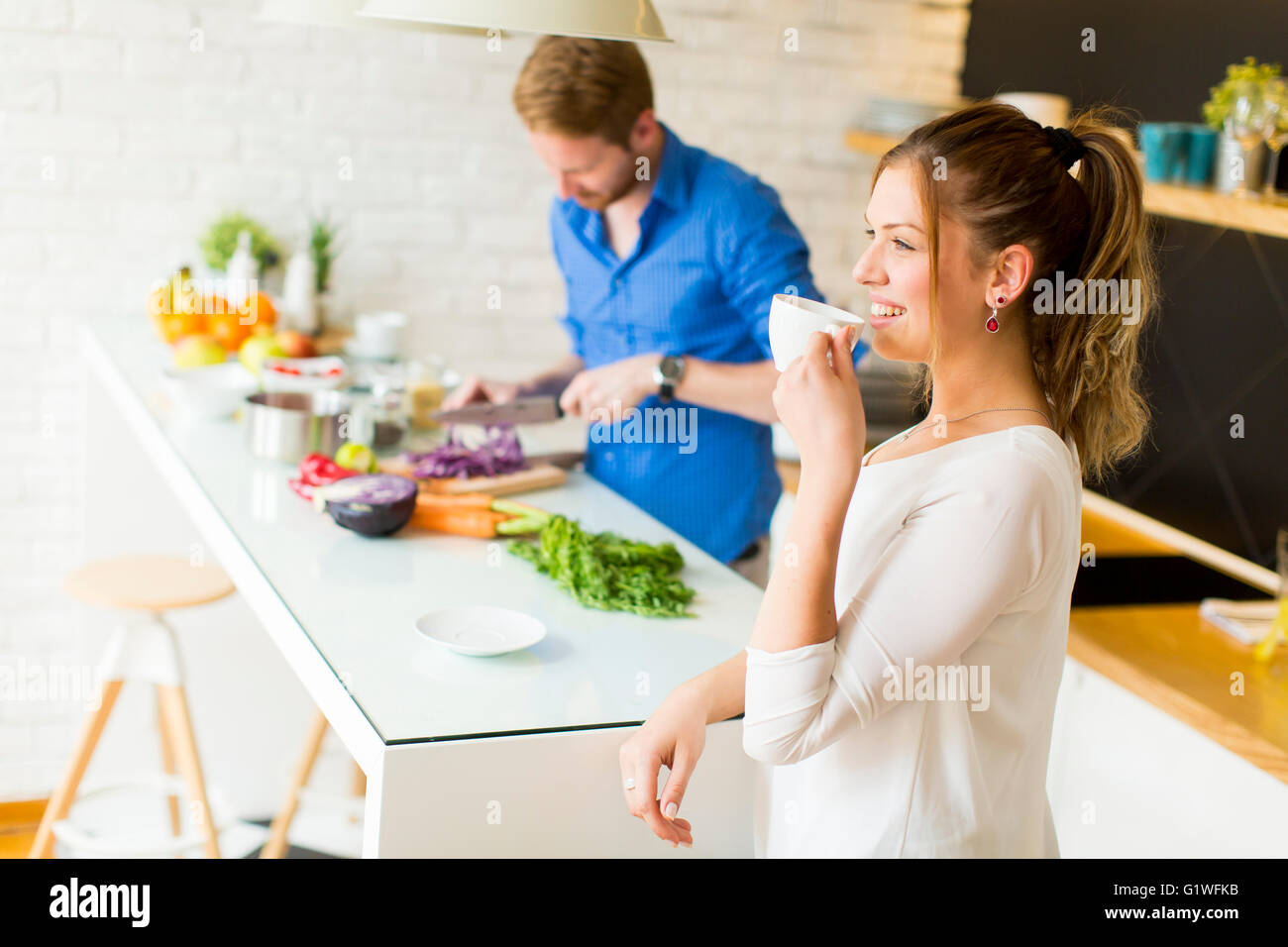 La donna beve caffè mentre un uomo si prepara un pasto Foto Stock
