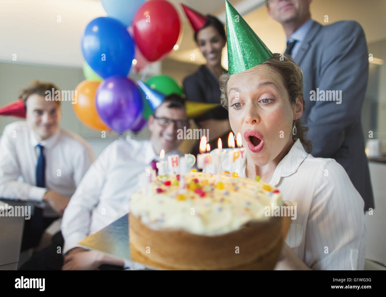 I colleghi guardando imprenditrice di soffiaggio in fuori la torta di compleanno candele Foto Stock