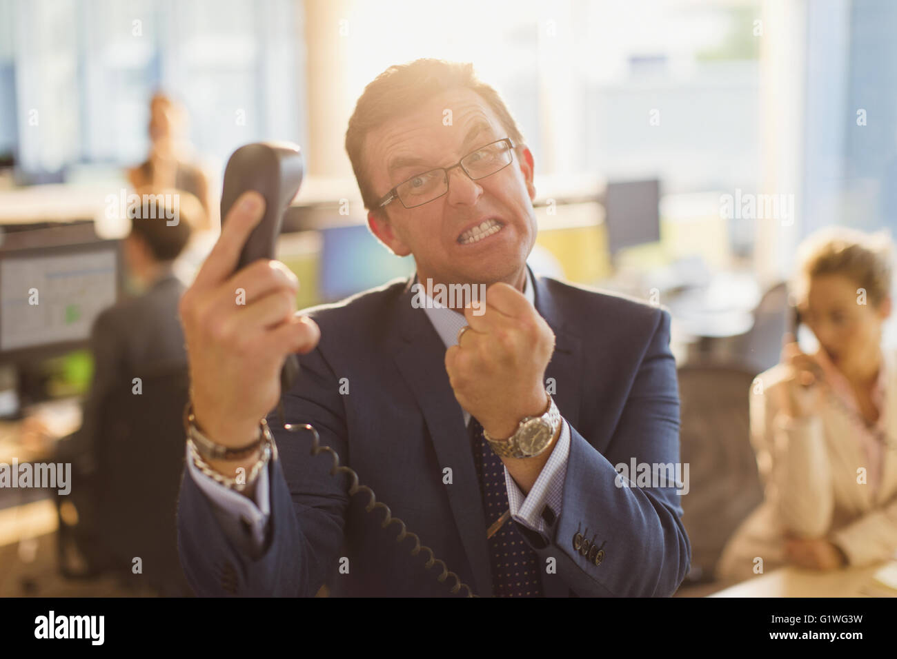 Furious imprenditore gesticolando con pugno al telefono in ufficio Foto Stock
