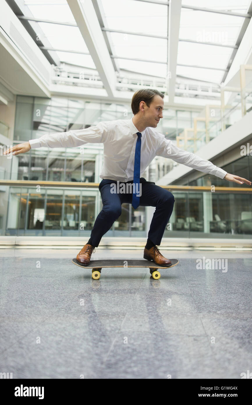 Imprenditore giocoso skateboarding in corridoio di office Foto Stock