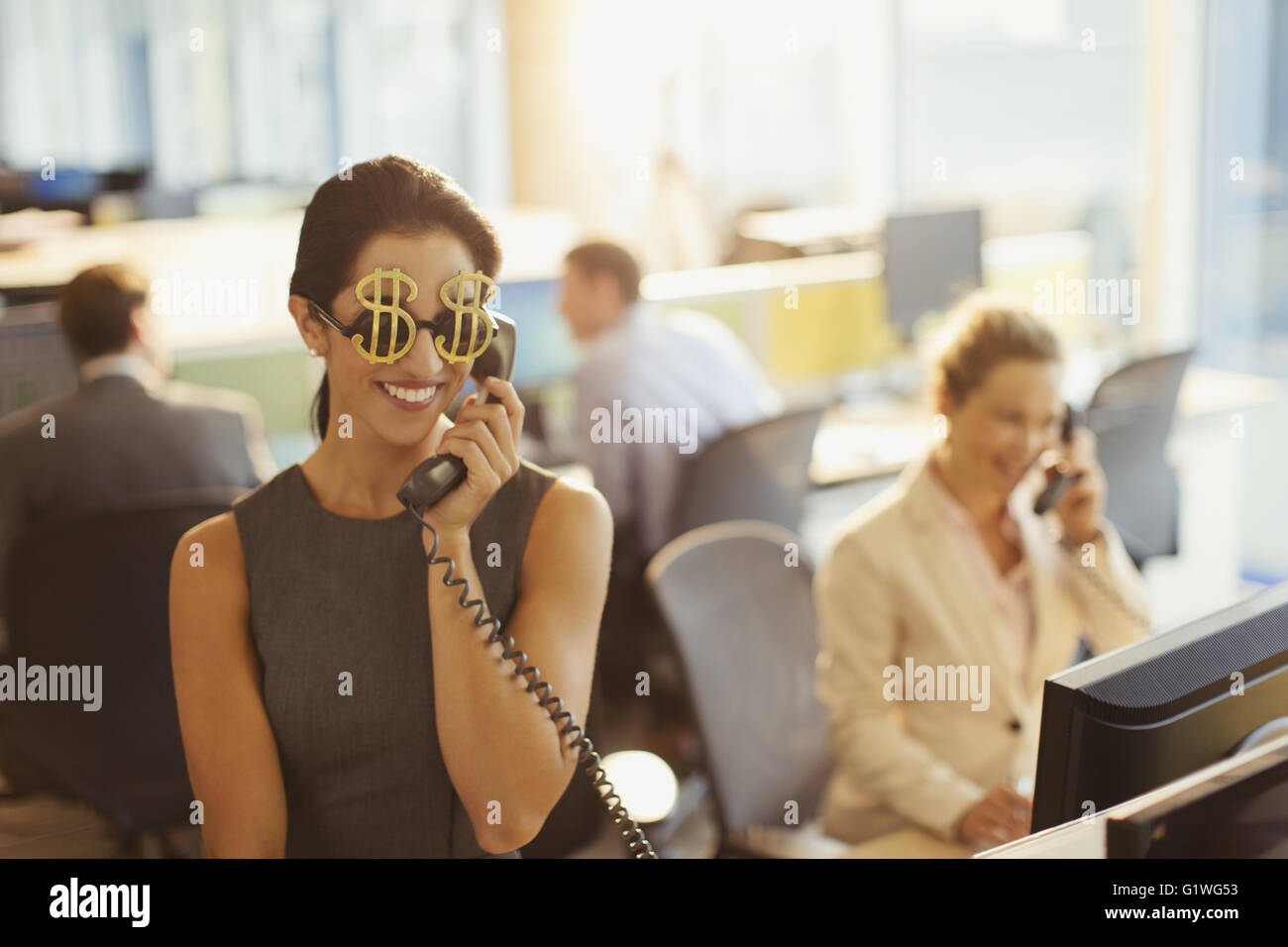 Ritratto di sorridere imprenditrice che indossa il simbolo del dollaro occhiali da sole rispondendo telefono in ufficio Foto Stock