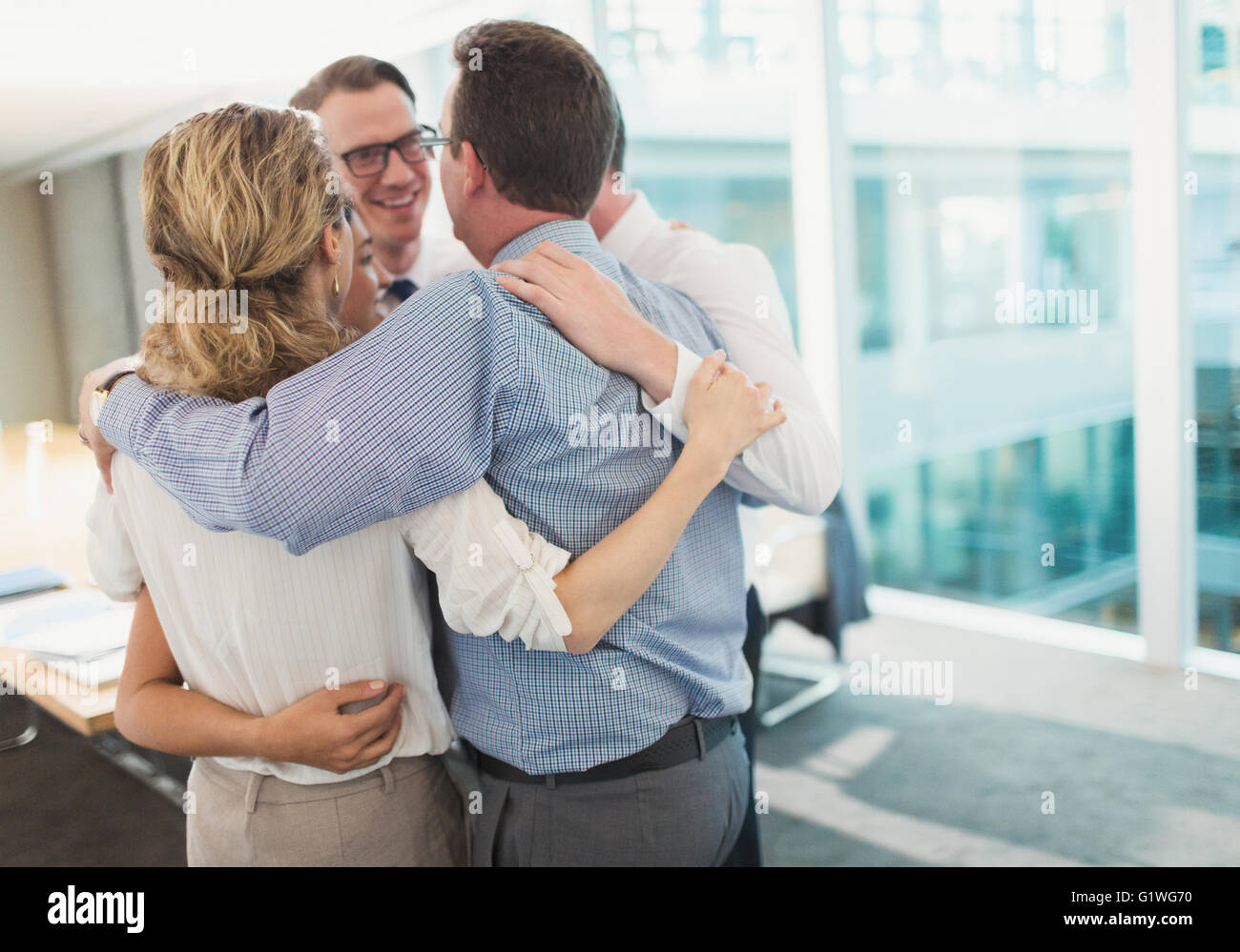 Sorridente la gente di affari abbracciando in huddle in sala conferenze Foto Stock