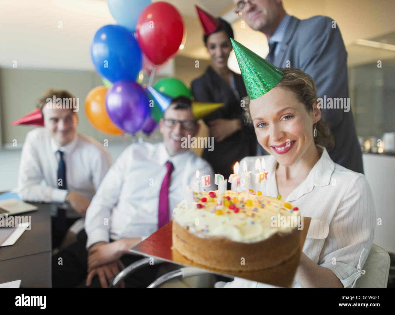Ritratto sorridente imprenditrice holding torta di compleanno con i colleghi in background Foto Stock