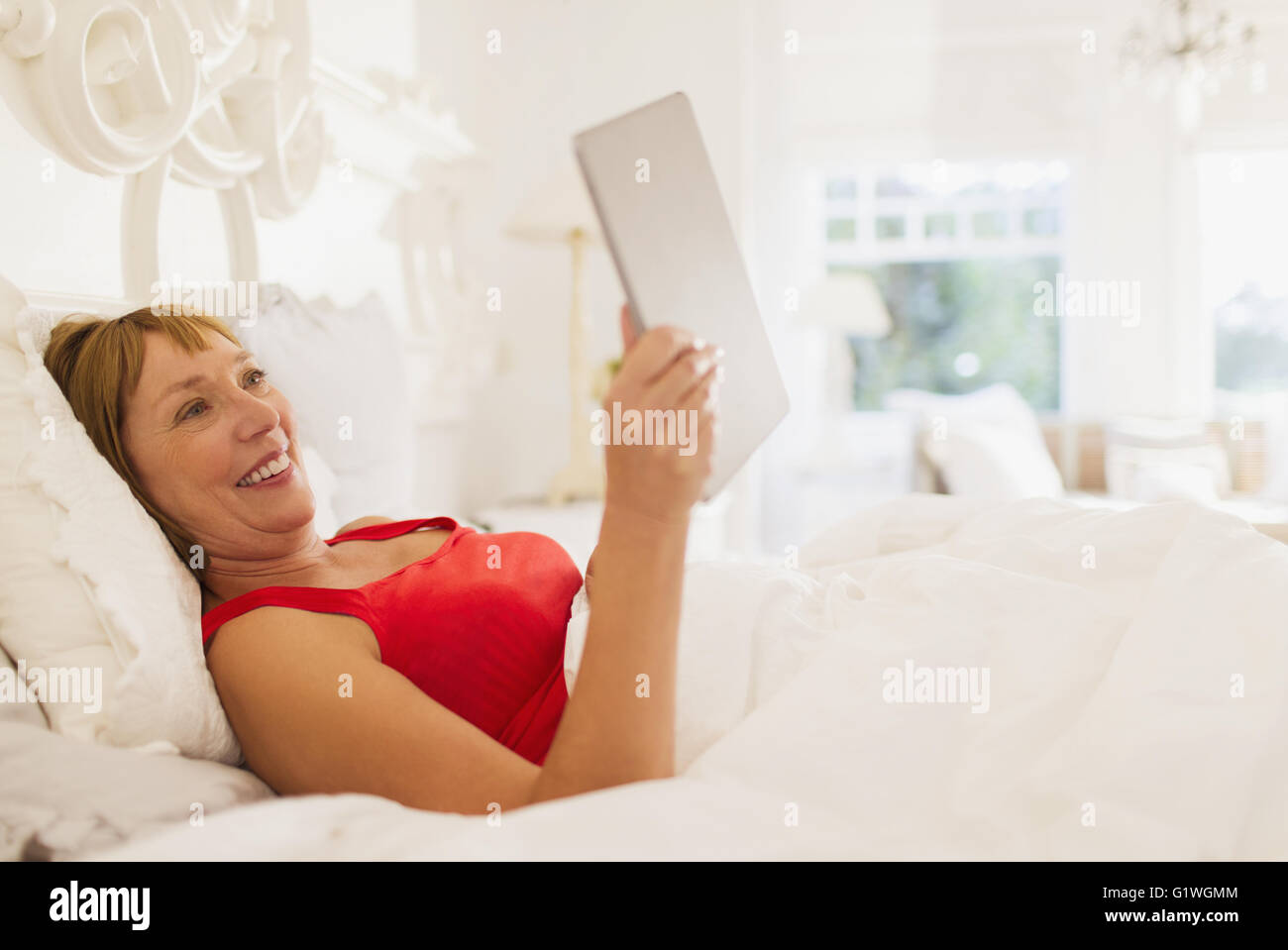 Sorridente donna matura con tavoletta digitale a letto Foto Stock