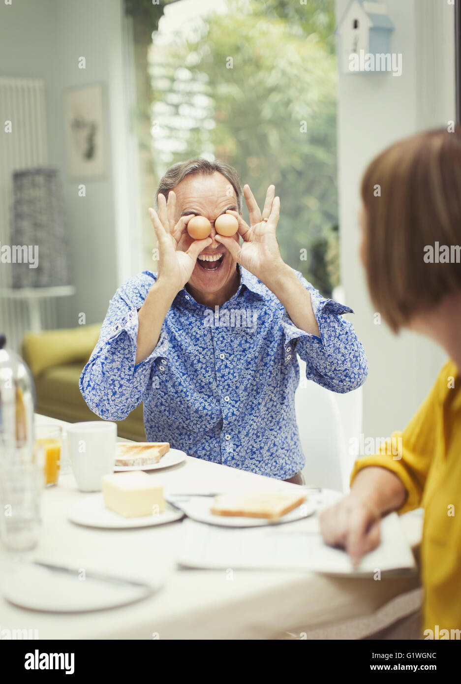 Giocoso uomo maturo che copre gli occhi con le uova al tavolo per la colazione Foto Stock