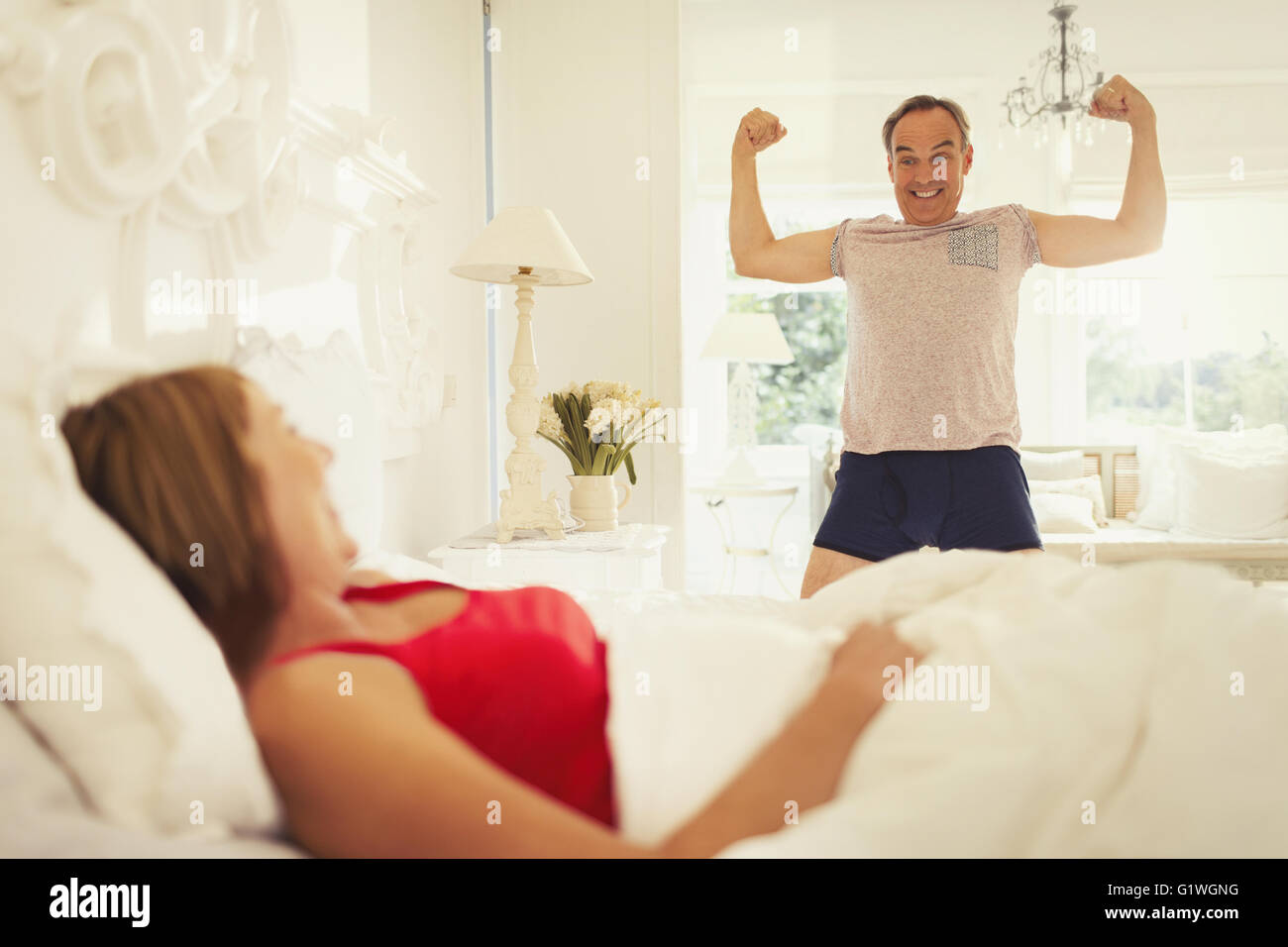 Giocoso uomo maturo la flessione dei muscoli per moglie in camera da letto Foto Stock