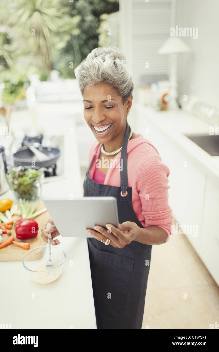 Sorridente donna matura con tavoletta digitale per la cottura in cucina Foto Stock
