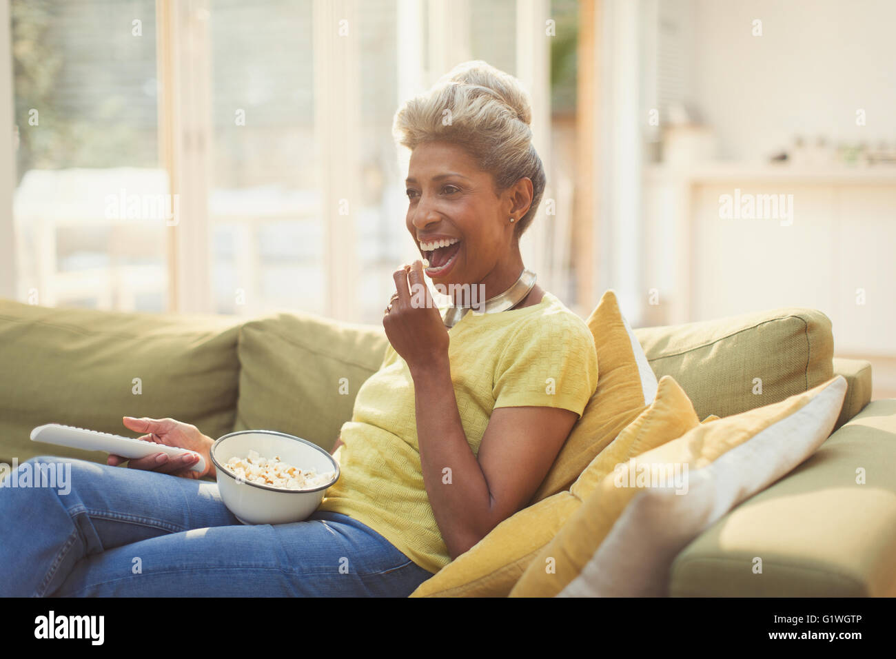 Donna matura mangiare popcorn e guardare la TV sul divano di casa Foto Stock