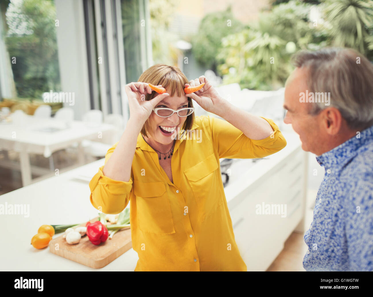 Giocoso donna matura gesti corni di carota in cucina Foto Stock