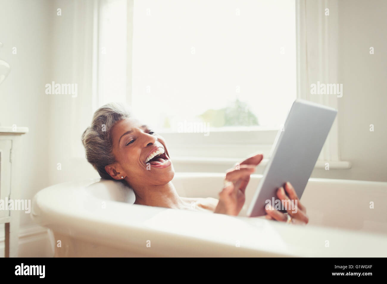 Ridendo donna matura con tavoletta digitale nella vasca da bagno Foto Stock