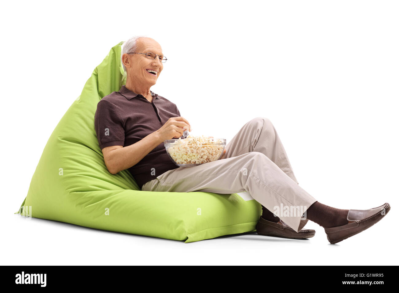 Senior gioiosa seduto su un verde beanbag e mangiare popcorn isolati su sfondo bianco Foto Stock